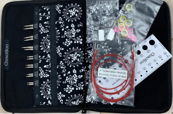 Knitting needle set with case, needles, cables, and accessories on a black background