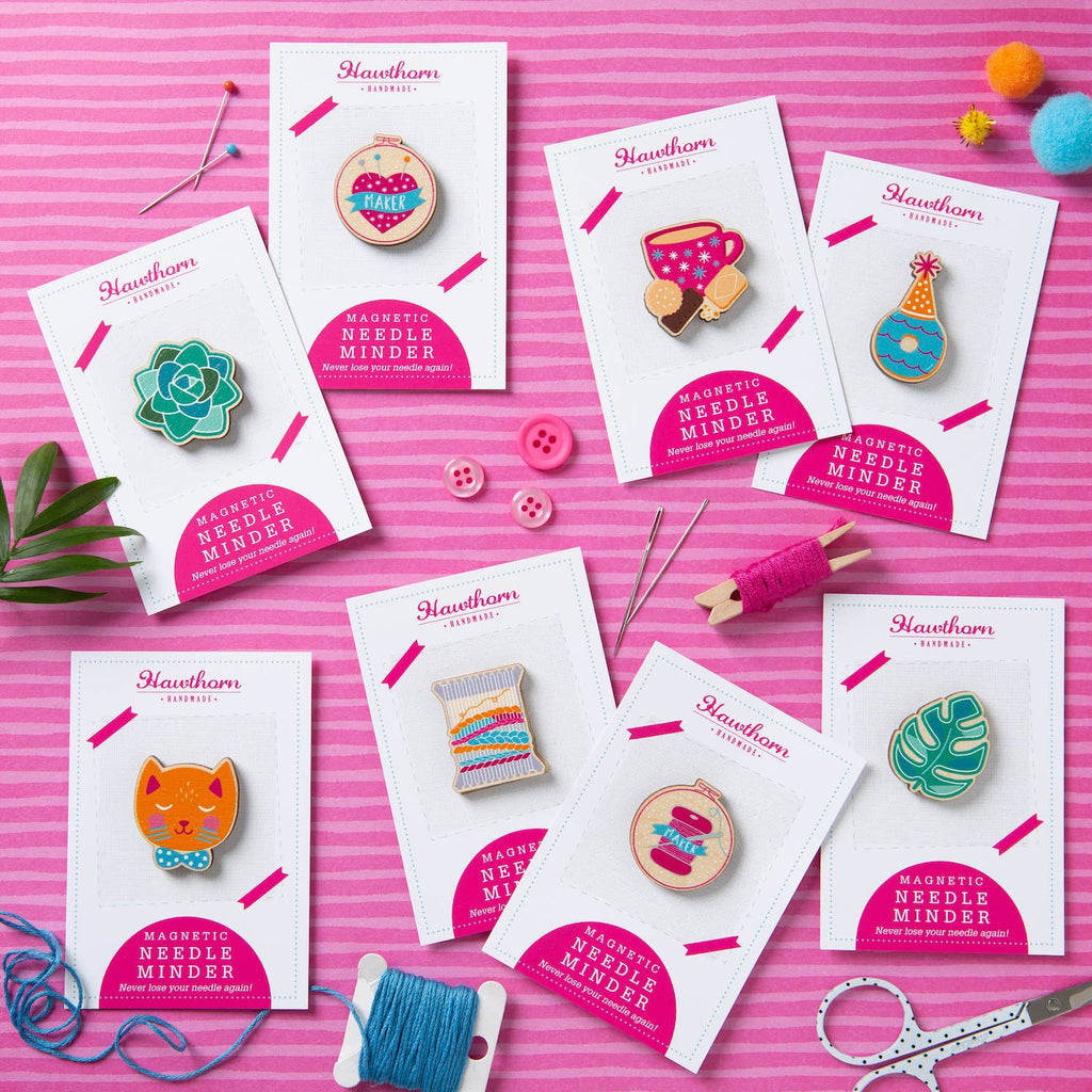Collection of Hawthorn Needle Minder products on a pink background with sewing tools.