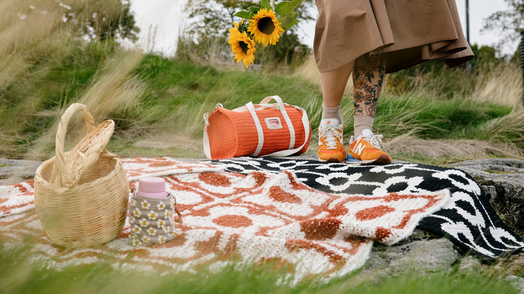 Person with an orange duffel bag and patterned blanket in a natural setting