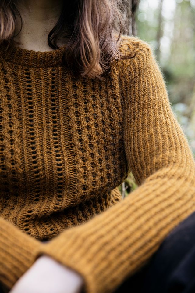 Close-up of a person wearing a mustard yellow knitted sweater with a blurred natural background.