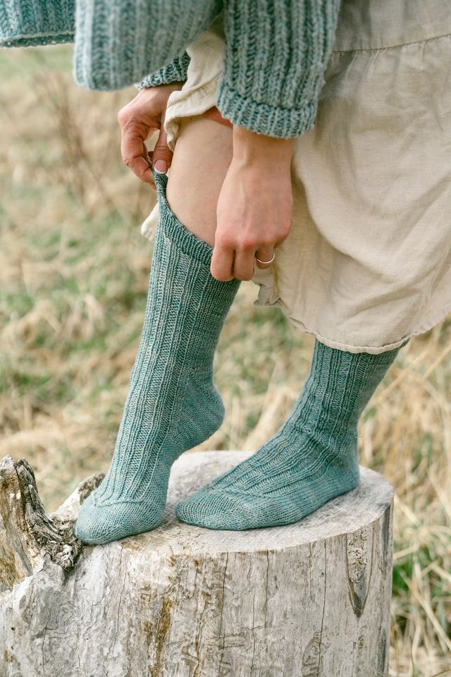 Person wearing green knitted socks standing on a wooden log with a natural background