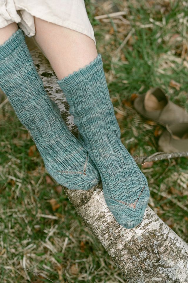Teal knitted socks on a person's feet with a blurred natural background