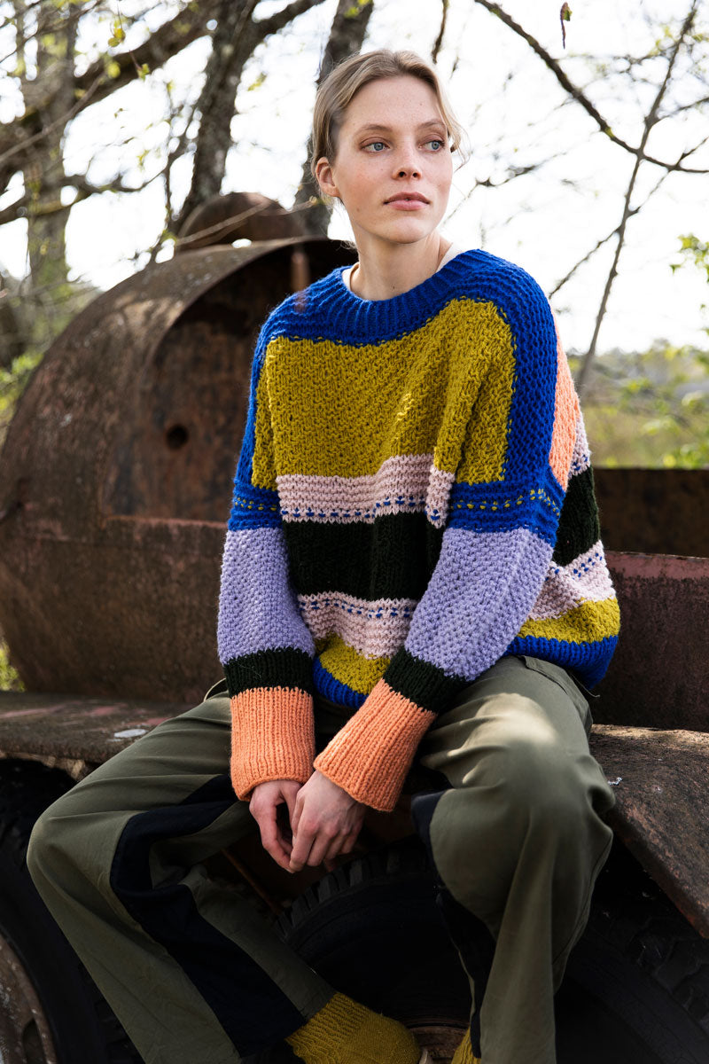 Person wearing a colorful striped sweater sitting outdoors.