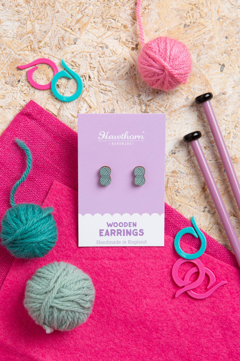 Hawthorn & Co wooden earrings with yarn balls and knitting needles on a textured surface