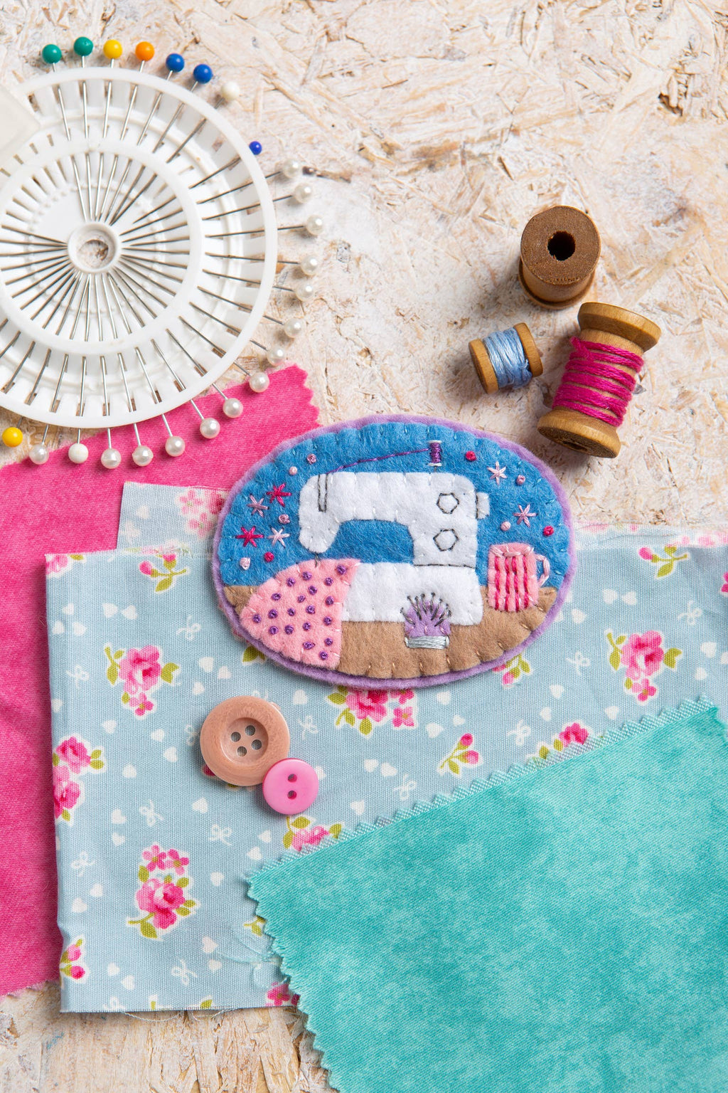 Sewing accessories including fabric, buttons, and a sewing machine brooch on a textured surface.