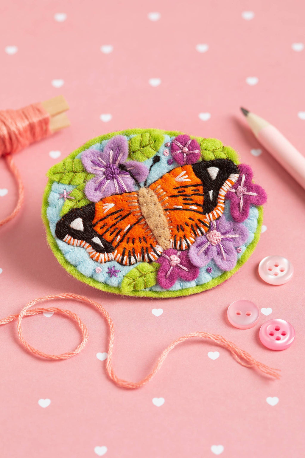 Embroidered butterfly brooch on a pink background with buttons and thread