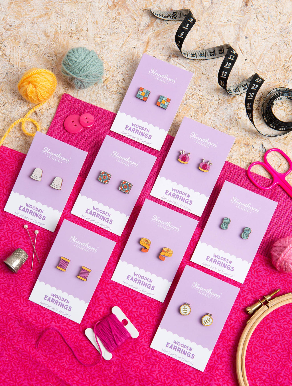 Wooden earrings on purple cards with crafting materials on a pink surface