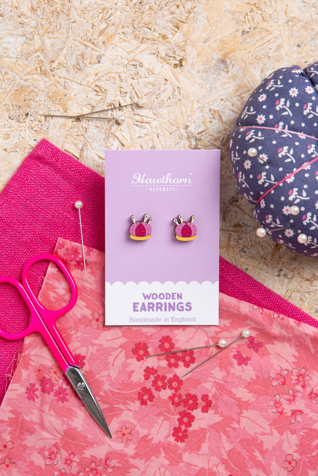 Hawthorn Wooden Earrings packaging on a textured surface with pink scissors and fabric.