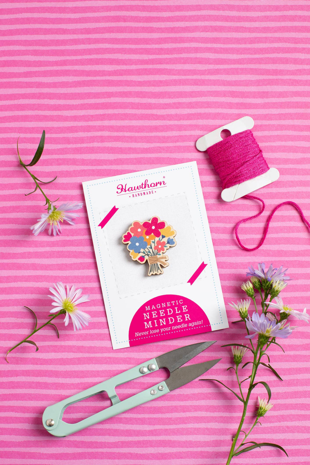 Hawthorn Magnetic Needle Minder on a pink striped background with flowers and thread spool.