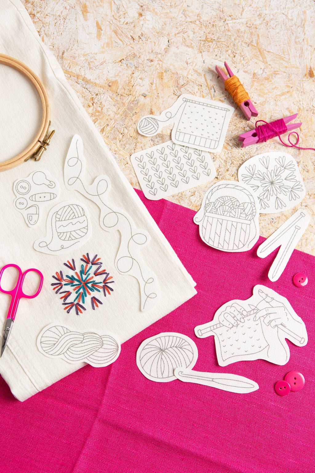 Embroidery patterns on fabric with scissors and thread on a pink surface