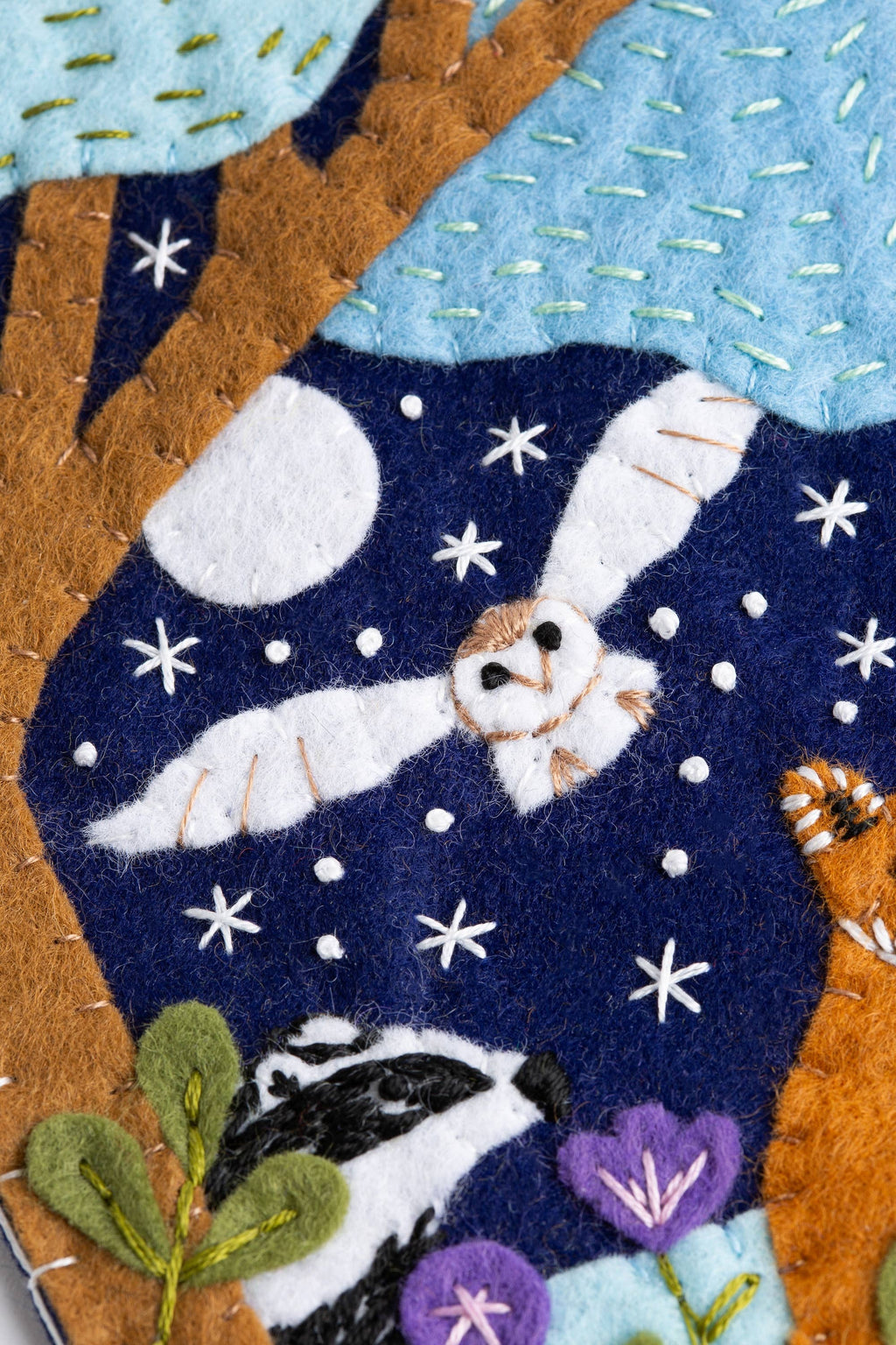 Felted artwork of animals under a starry sky with trees and flowers.