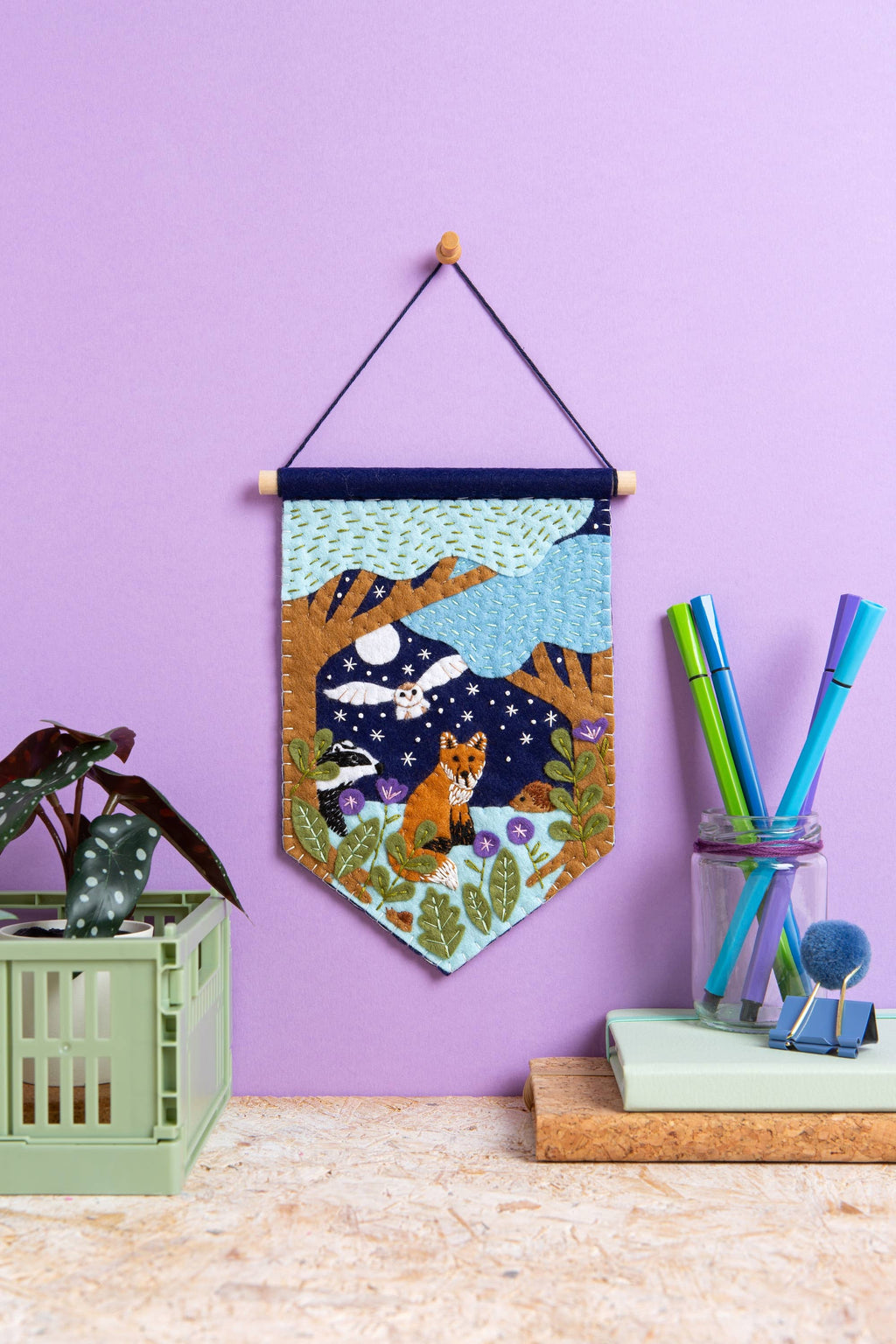 Decorative wall hanging with fox design on a purple wall, with stationery items below.