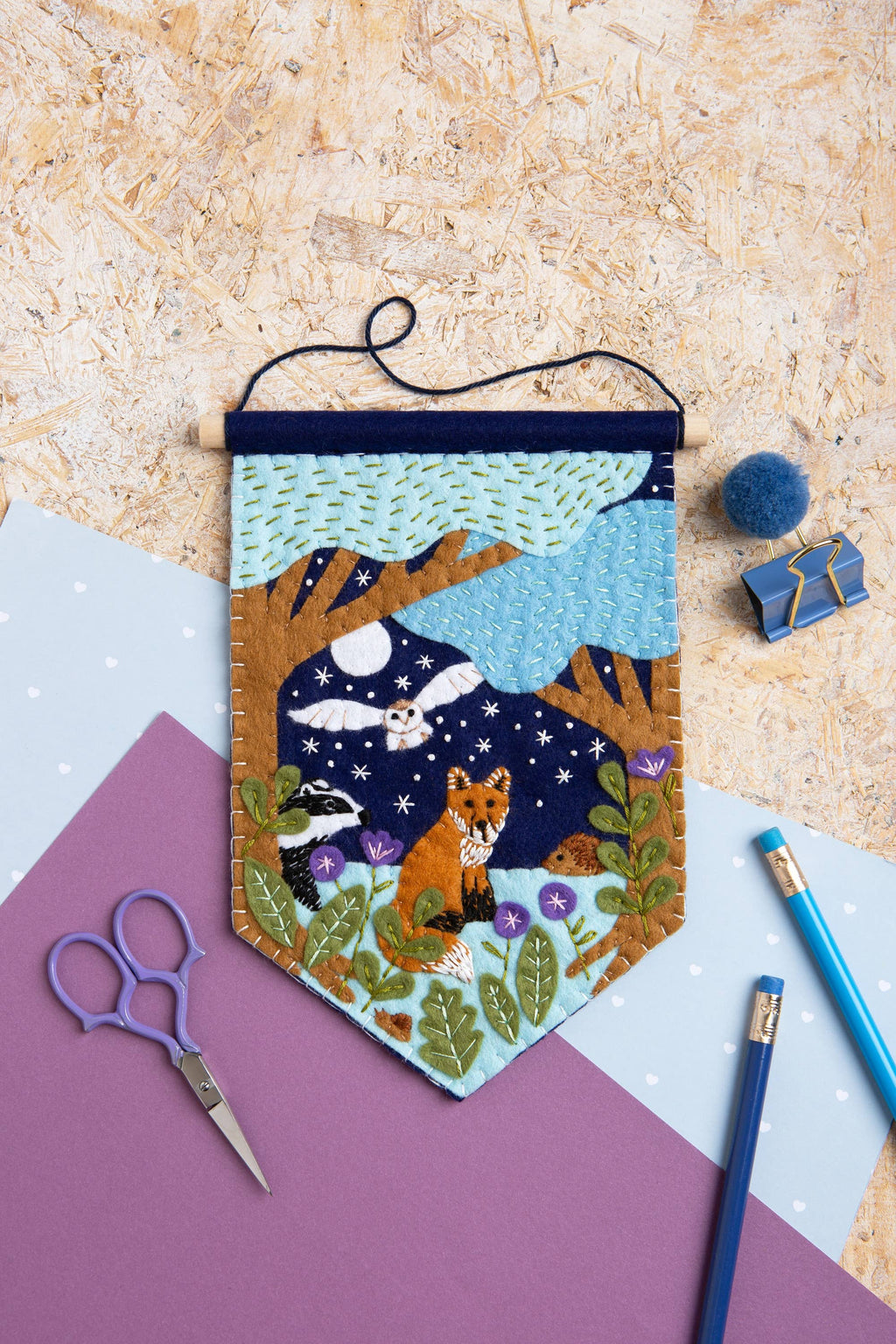 Handmade wall hanging with fox design on a textured surface with crafting tools.