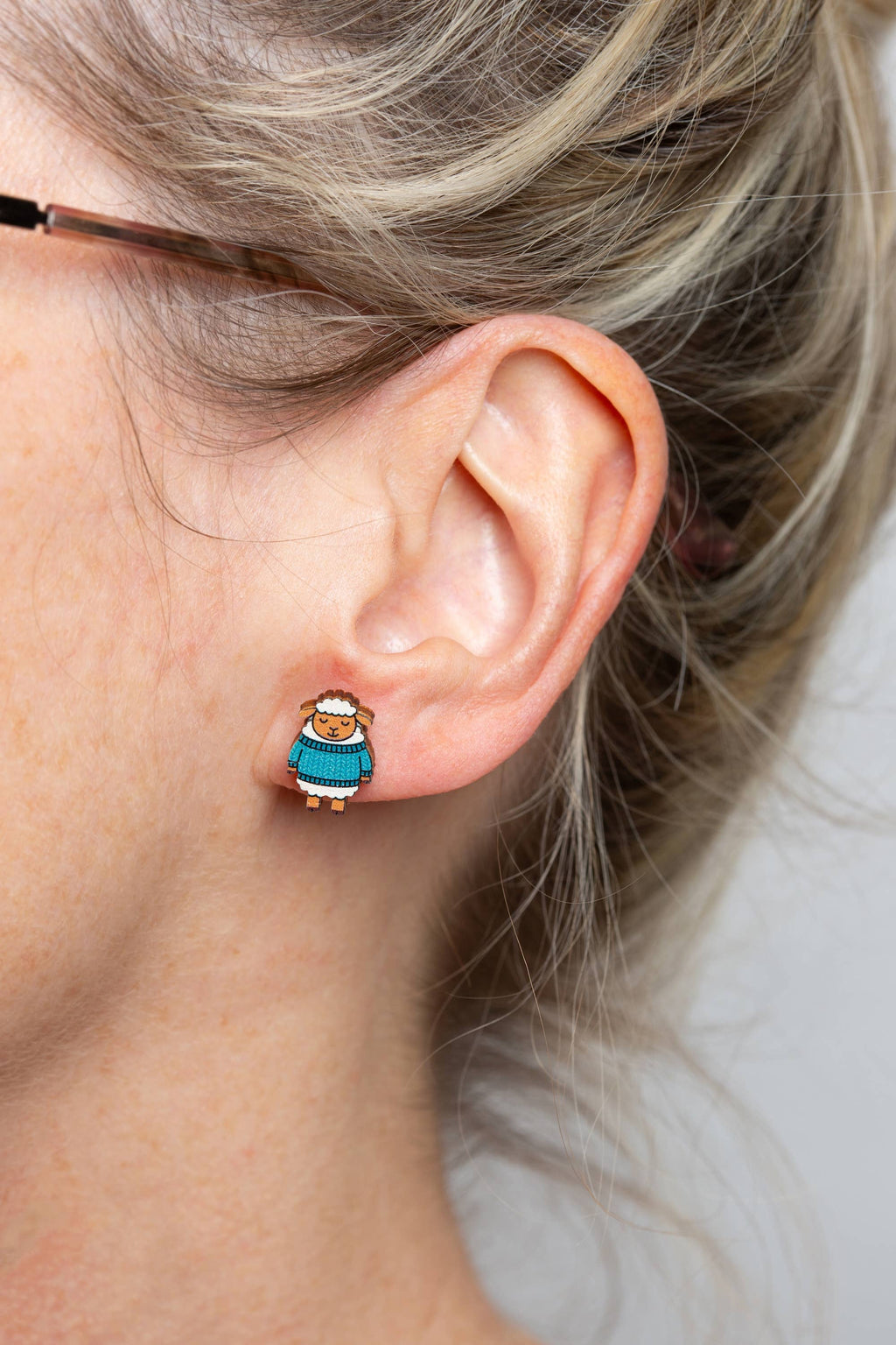 Close-up of an ear wearing a small earring with a character design, with a neutral background.
