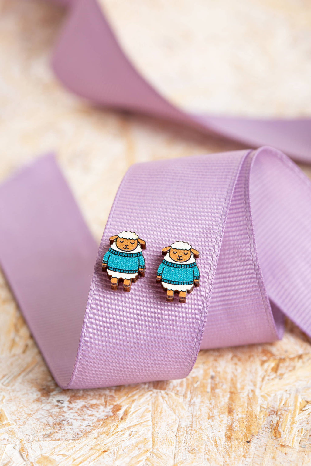 Sheep-shaped earrings on a purple ribbon with a textured beige background