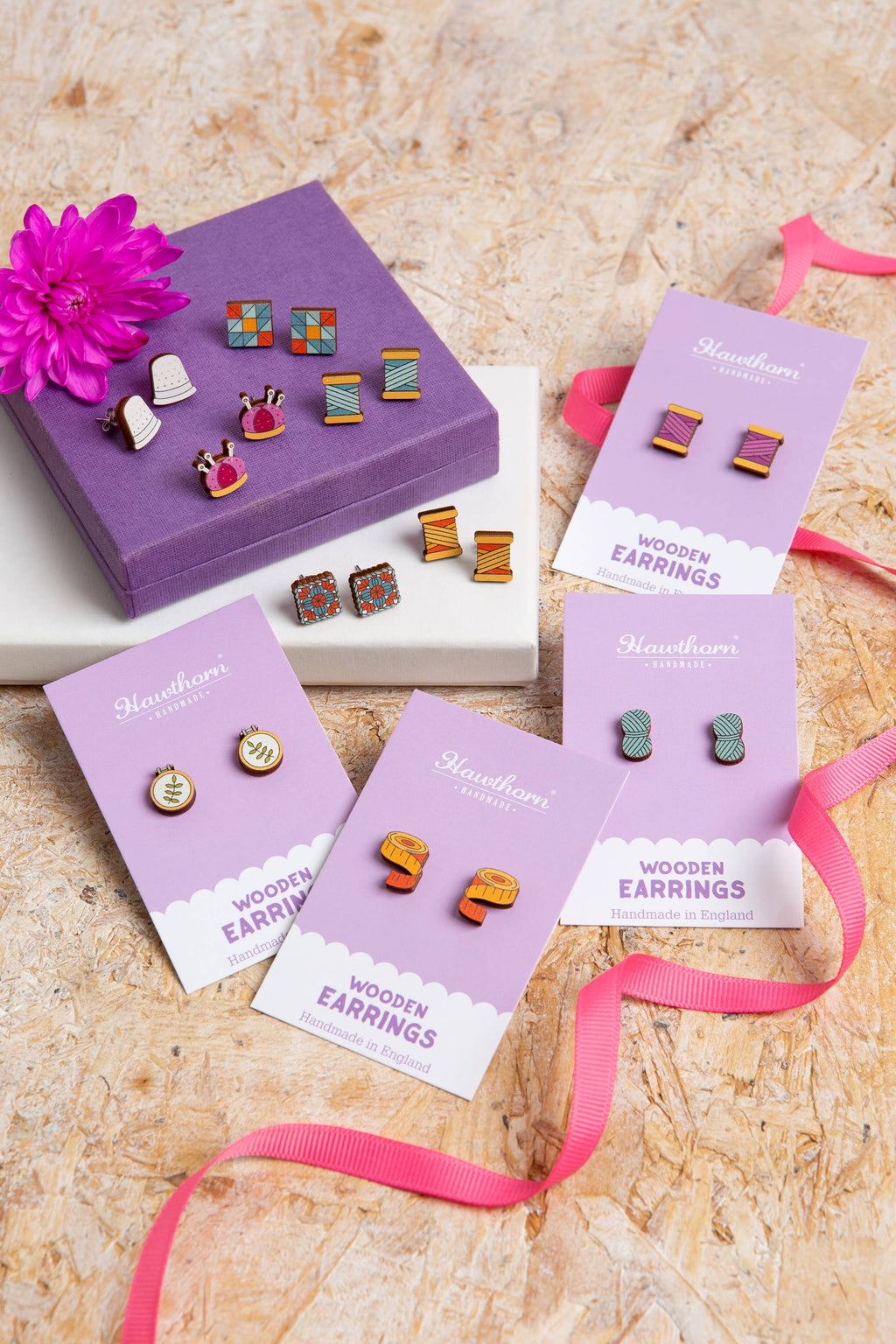 Wooden earrings in purple packaging on a textured surface with pink ribbons.
