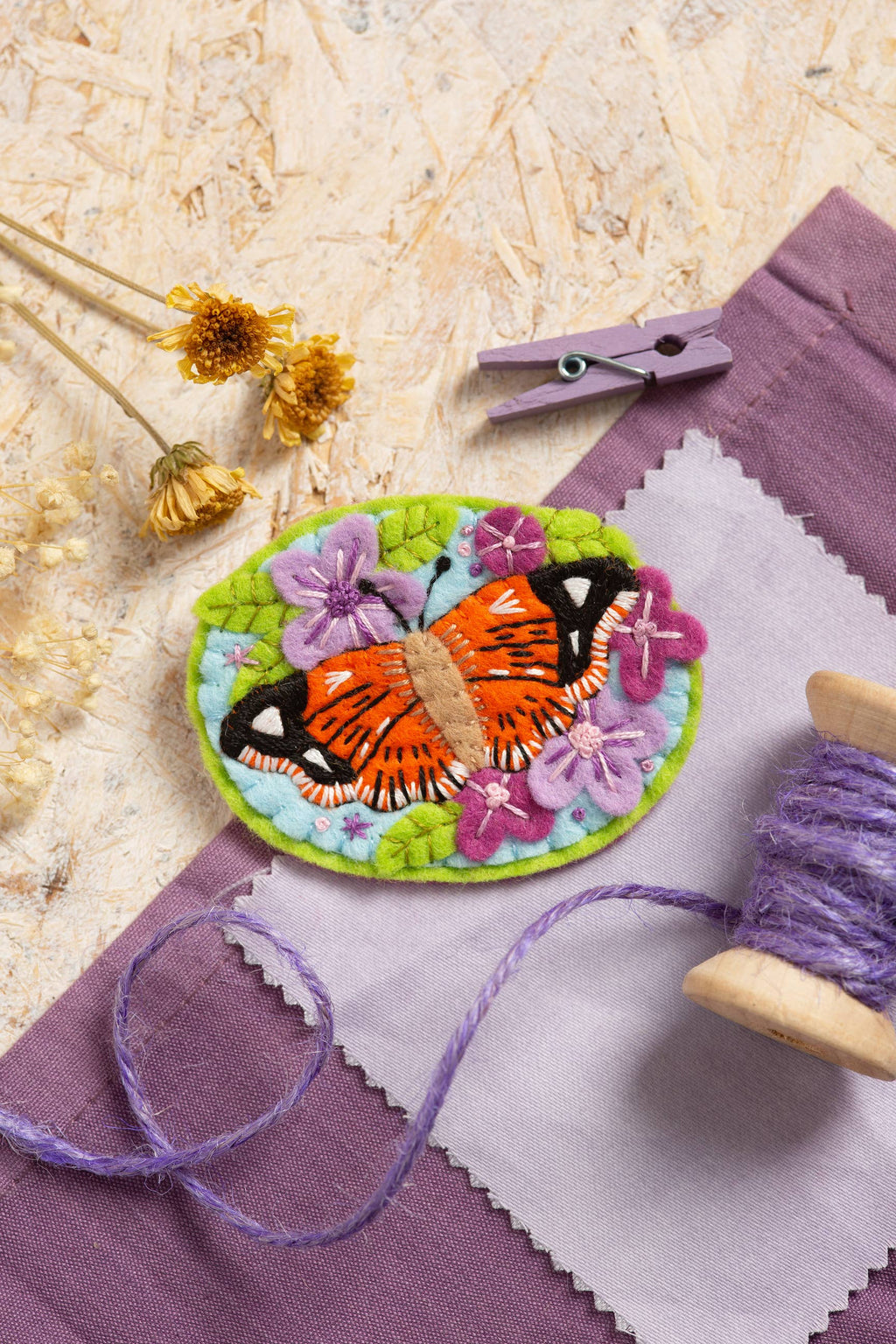 Embroidered butterfly brooch on fabric with a purple thread spool and wooden clip.