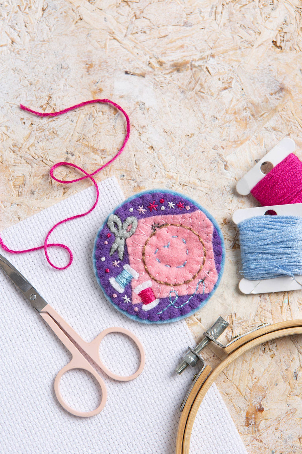 Embroidery hoop, scissors, and colorful thread on a textured surface with a completed embroidery design.