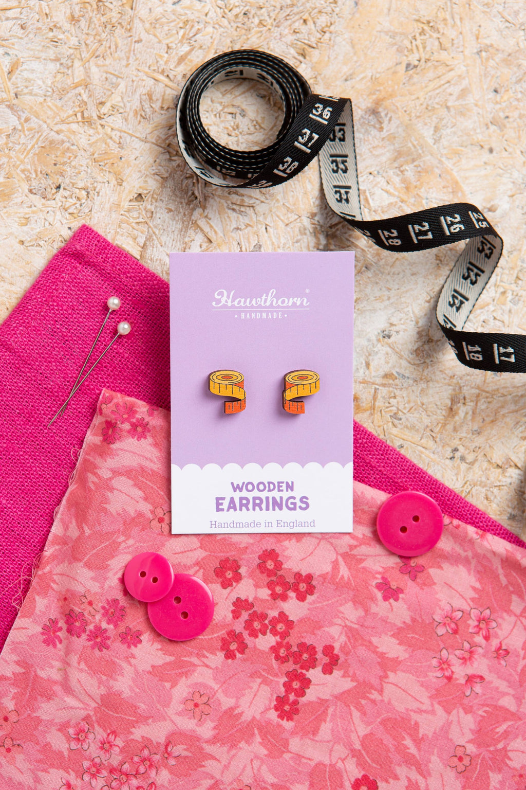 Wooden earrings in a box with pink fabric and measuring tape on a textured surface