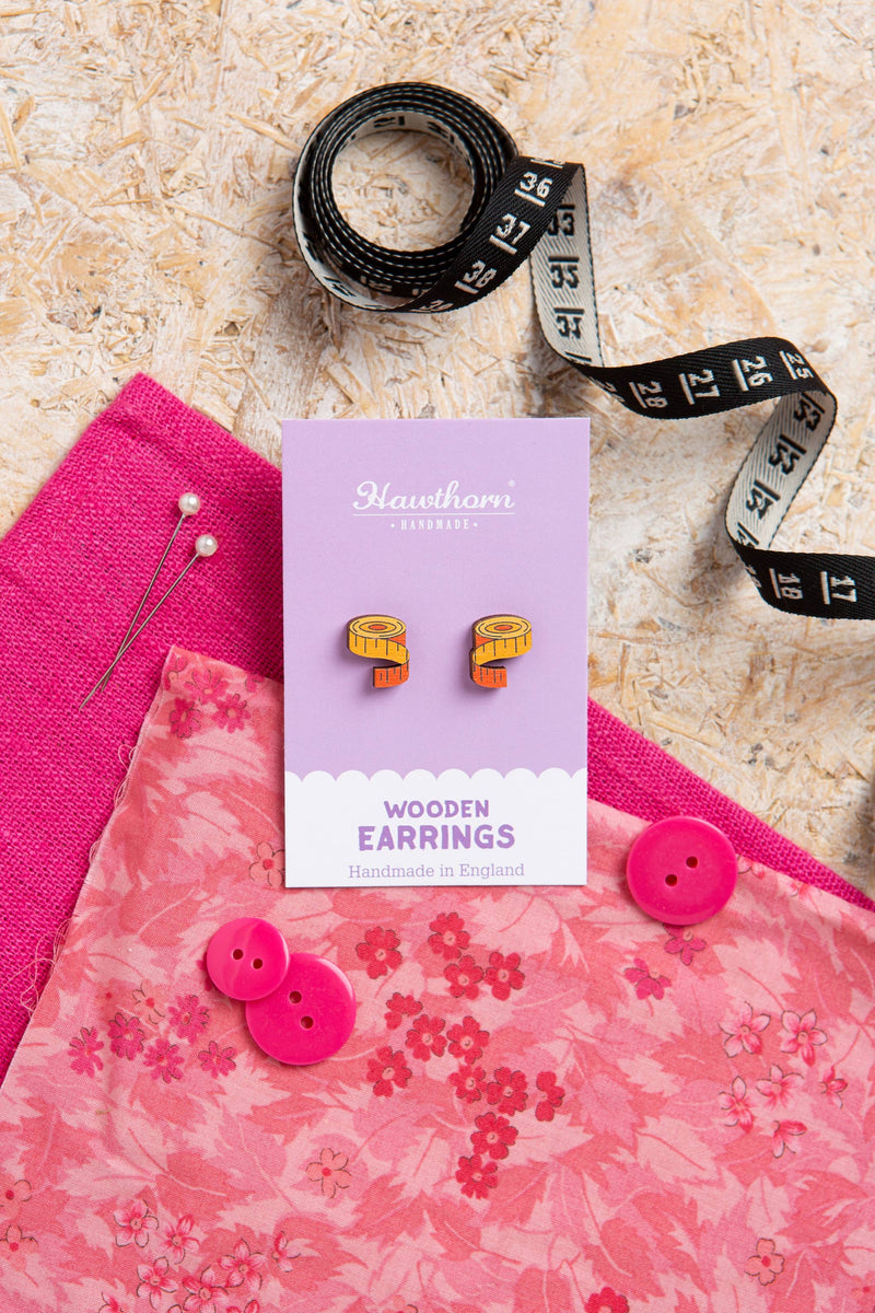 Wooden earrings in a box with pink fabric and measuring tape on a textured surface