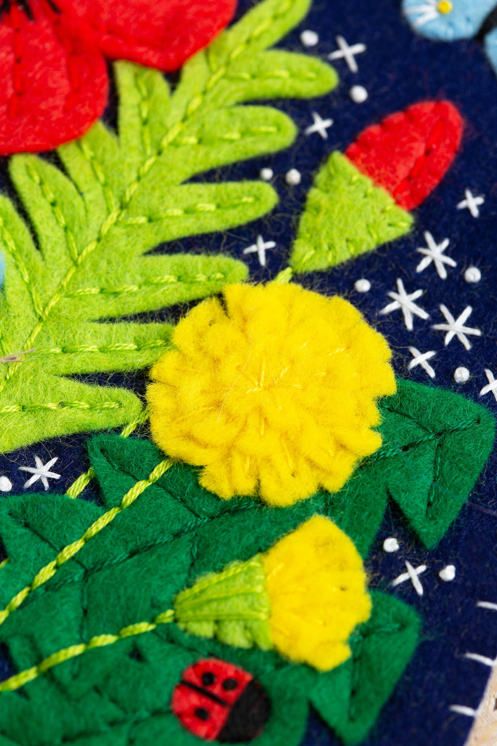 Embroidered patch with yellow flowers, green leaves, and a red ladybug on a dark background.