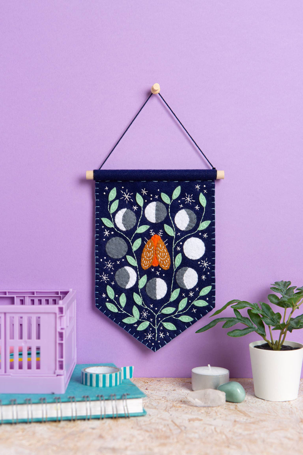 Decorative wall hanging with moon phases and a butterfly on a purple wall.