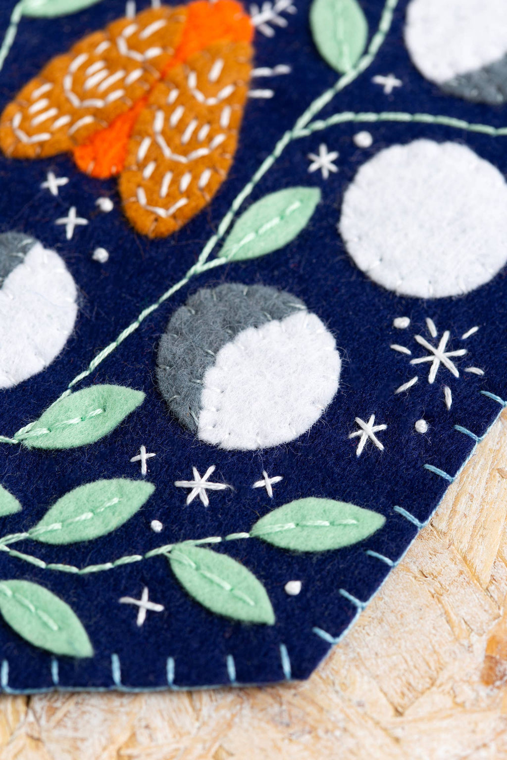 Felted fabric with embroidered design of leaves, berries, and stars on a dark blue background.