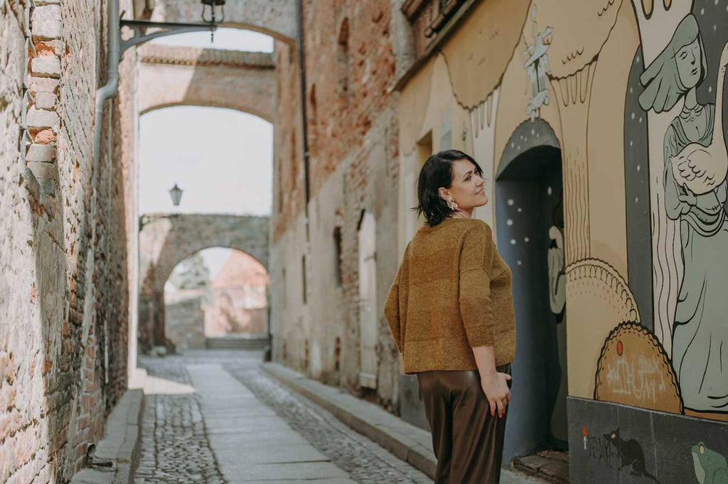 Woman standing in a narrow alleyway with a mural on a building wall.