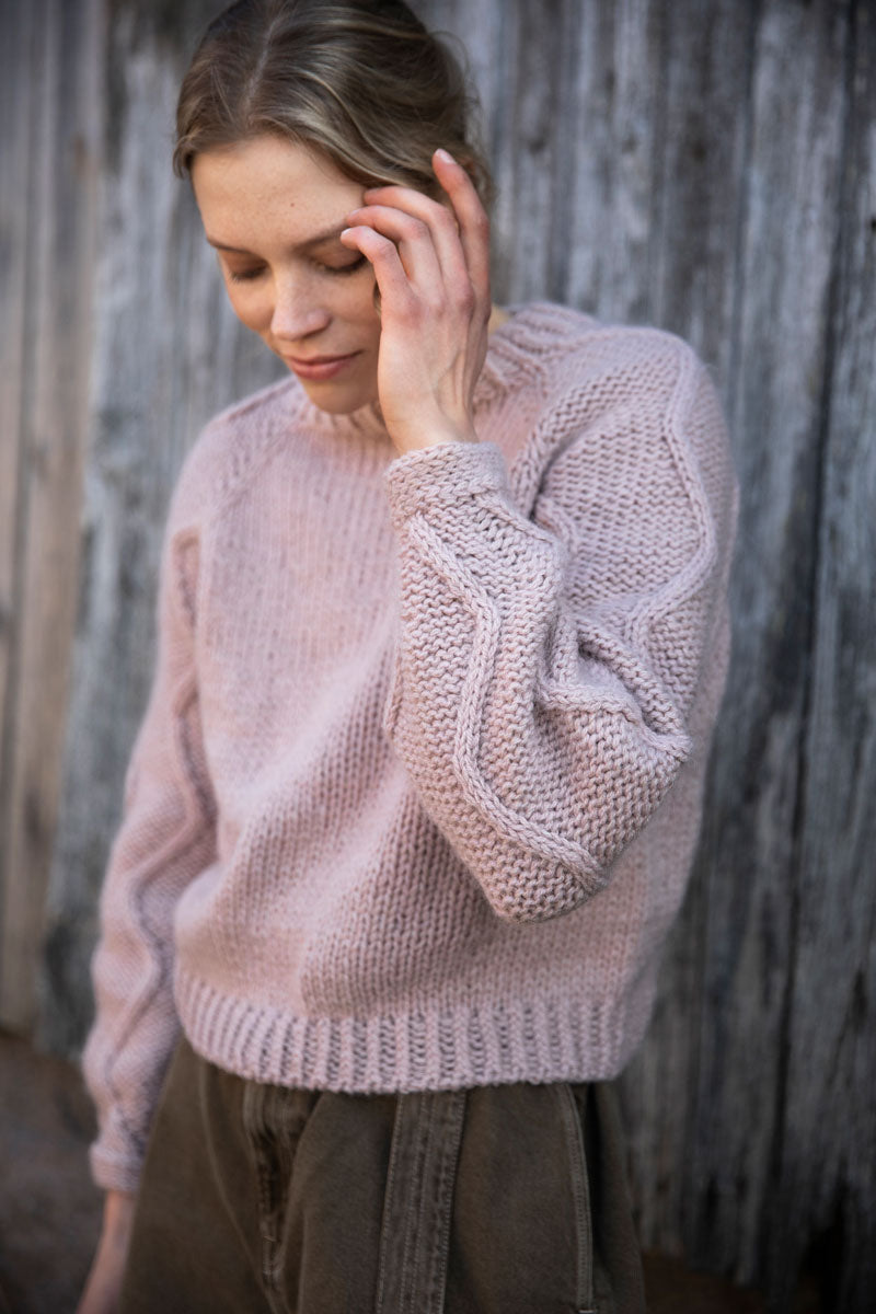 Woman wearing a light pink knitted sweater against a wooden background