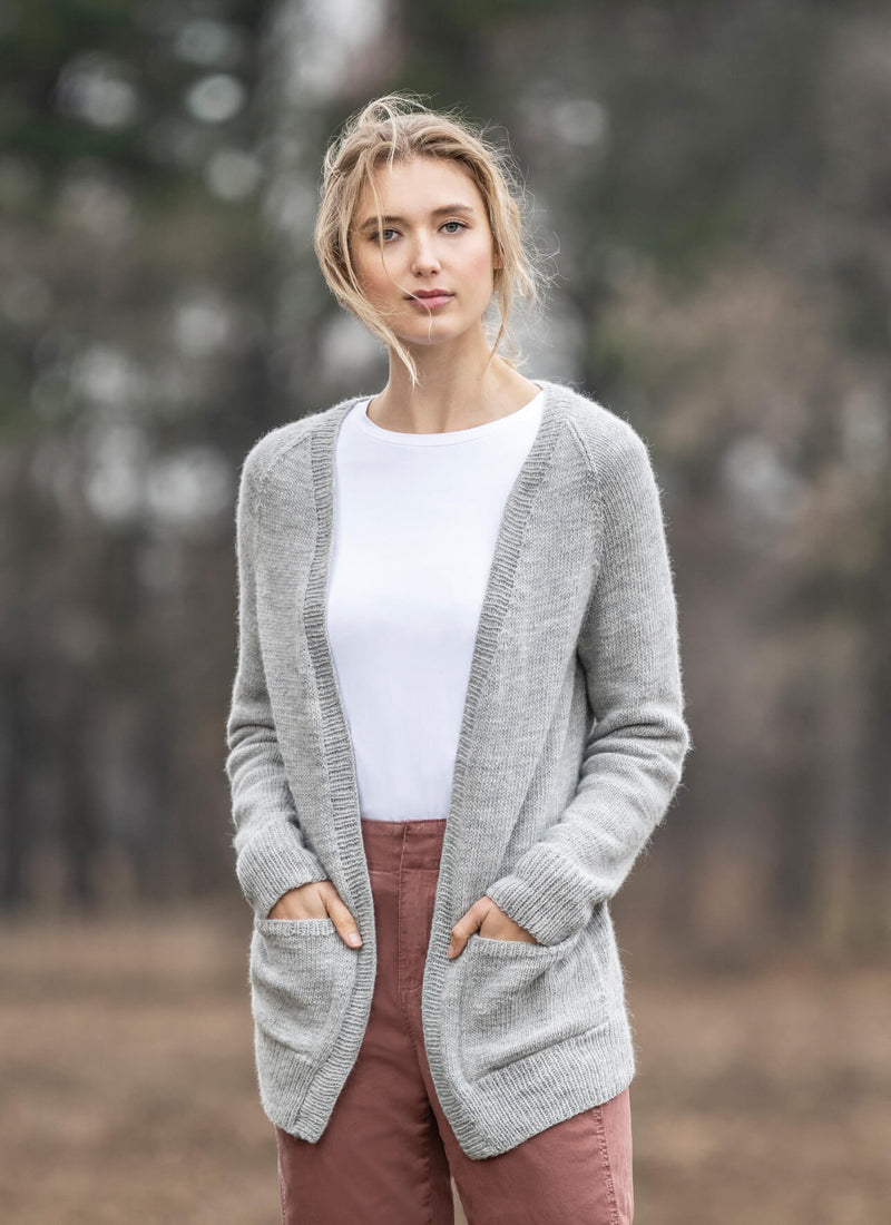 Woman wearing a gray cardigan over a white shirt and pink pants in a forest setting