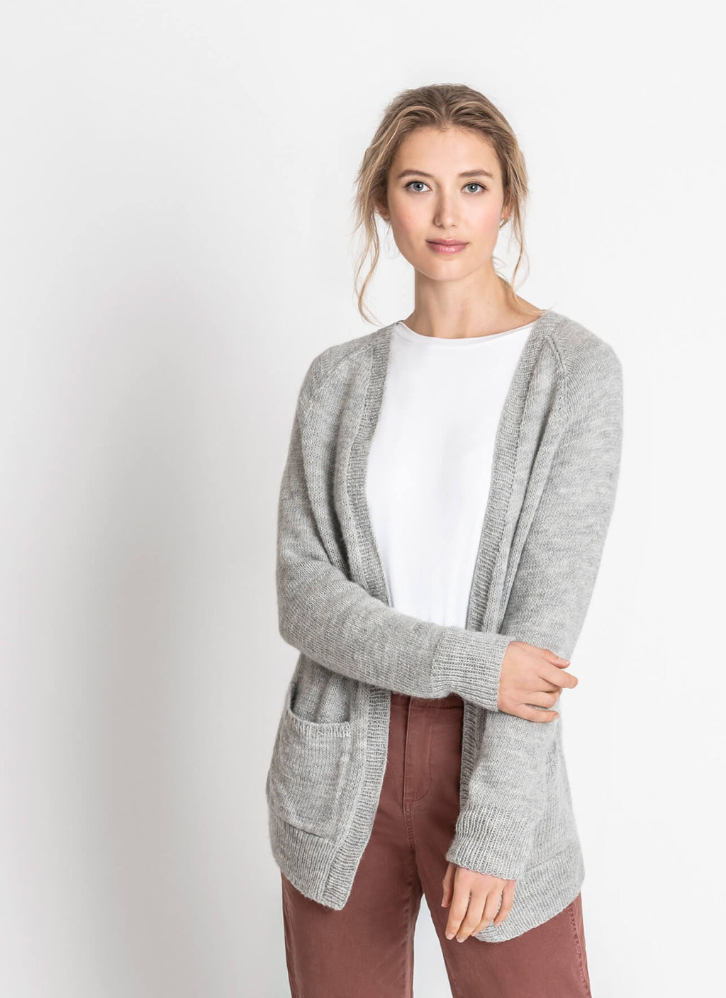 Woman wearing a gray cardigan over a white shirt with maroon pants on a light gray background