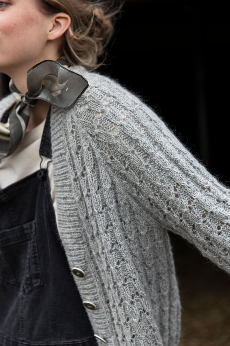 Person wearing a gray knitted cardigan with a dark background