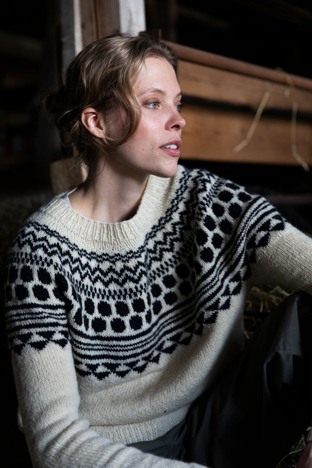 Woman wearing a patterned sweater sitting indoors.
