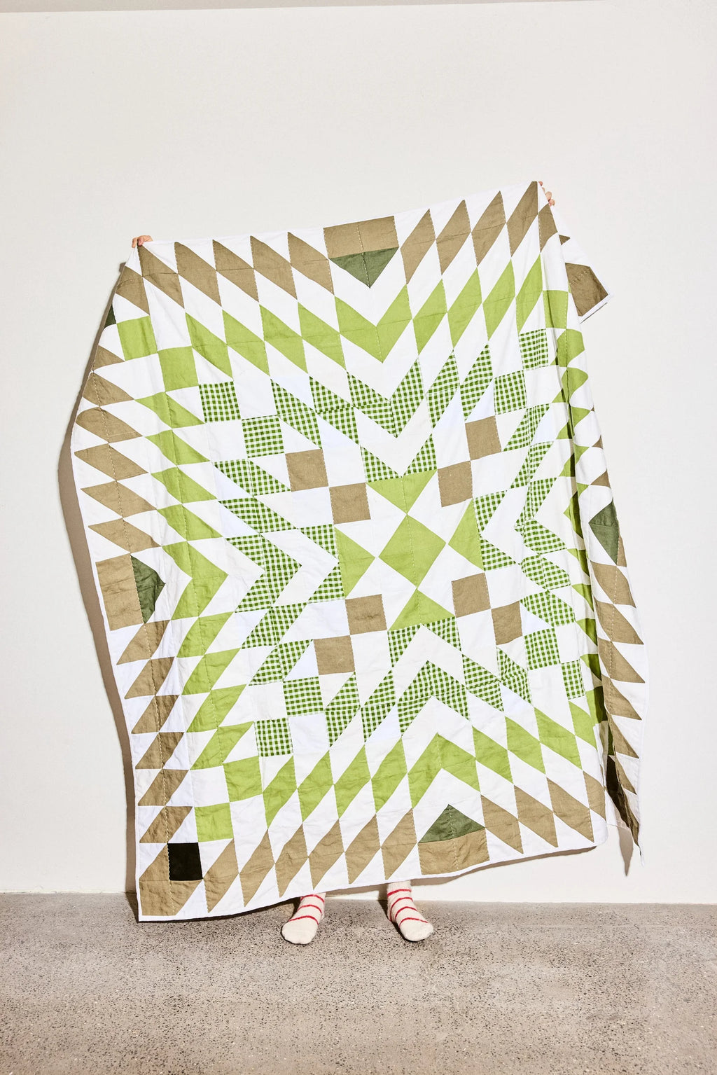 Quilt with geometric pattern draped over a person on a plain background