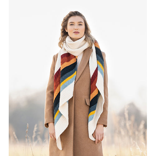 Woman wearing a colourful hand knit scarf and brown coat with a blurred natural background