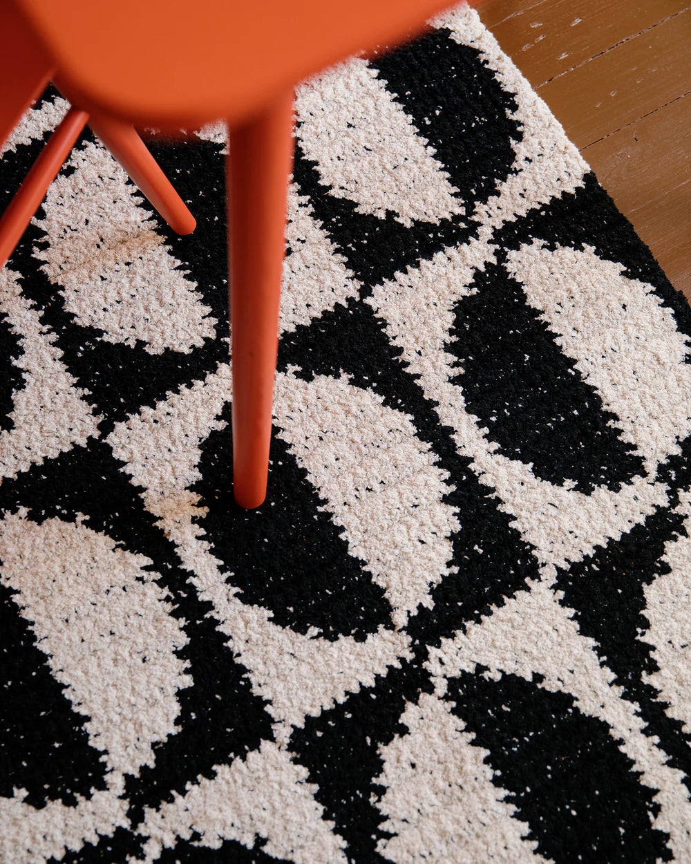 Black and white patterned rug with a red chair leg on a wooden floor.