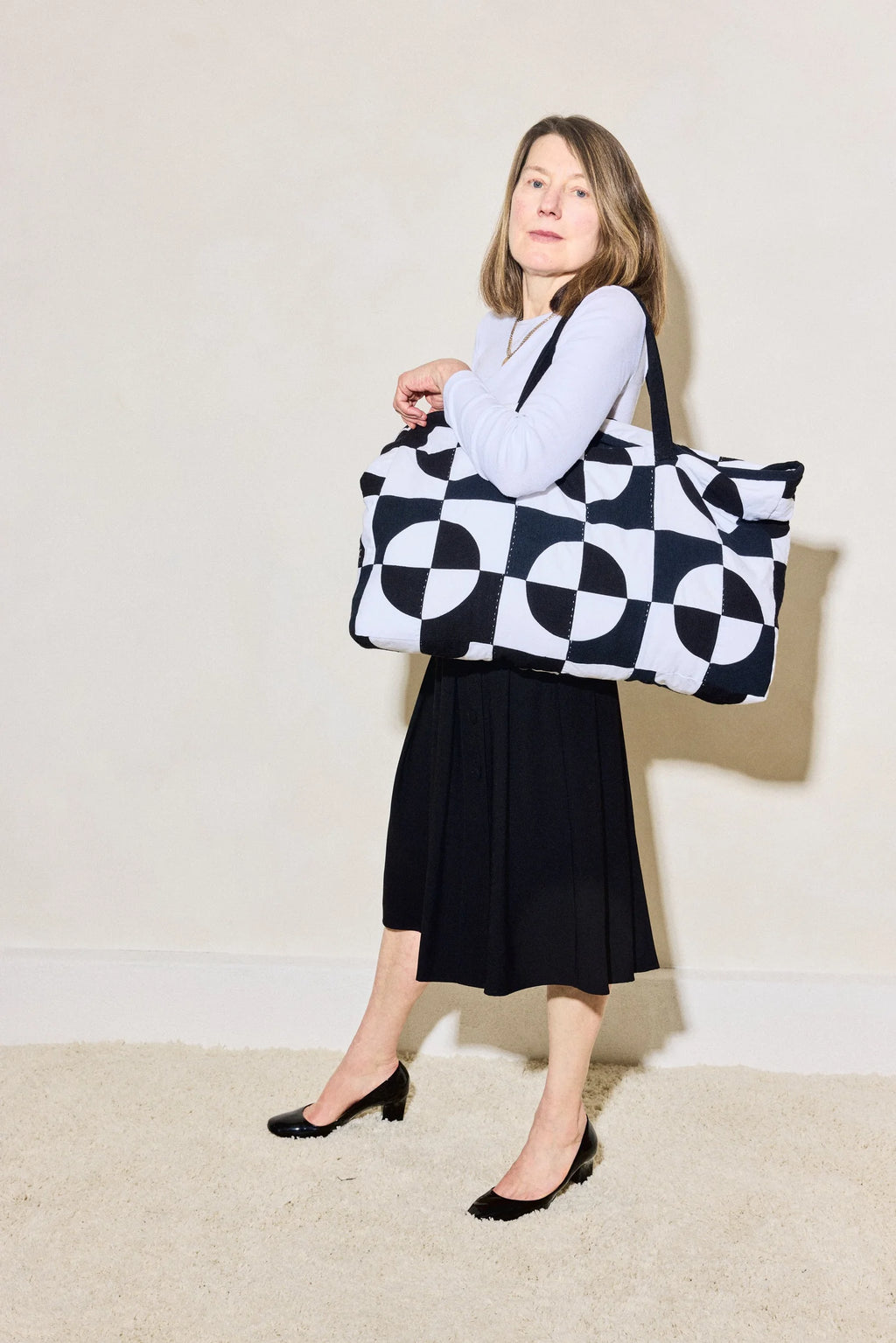 Woman holding a black and white patterned bag against a plain background