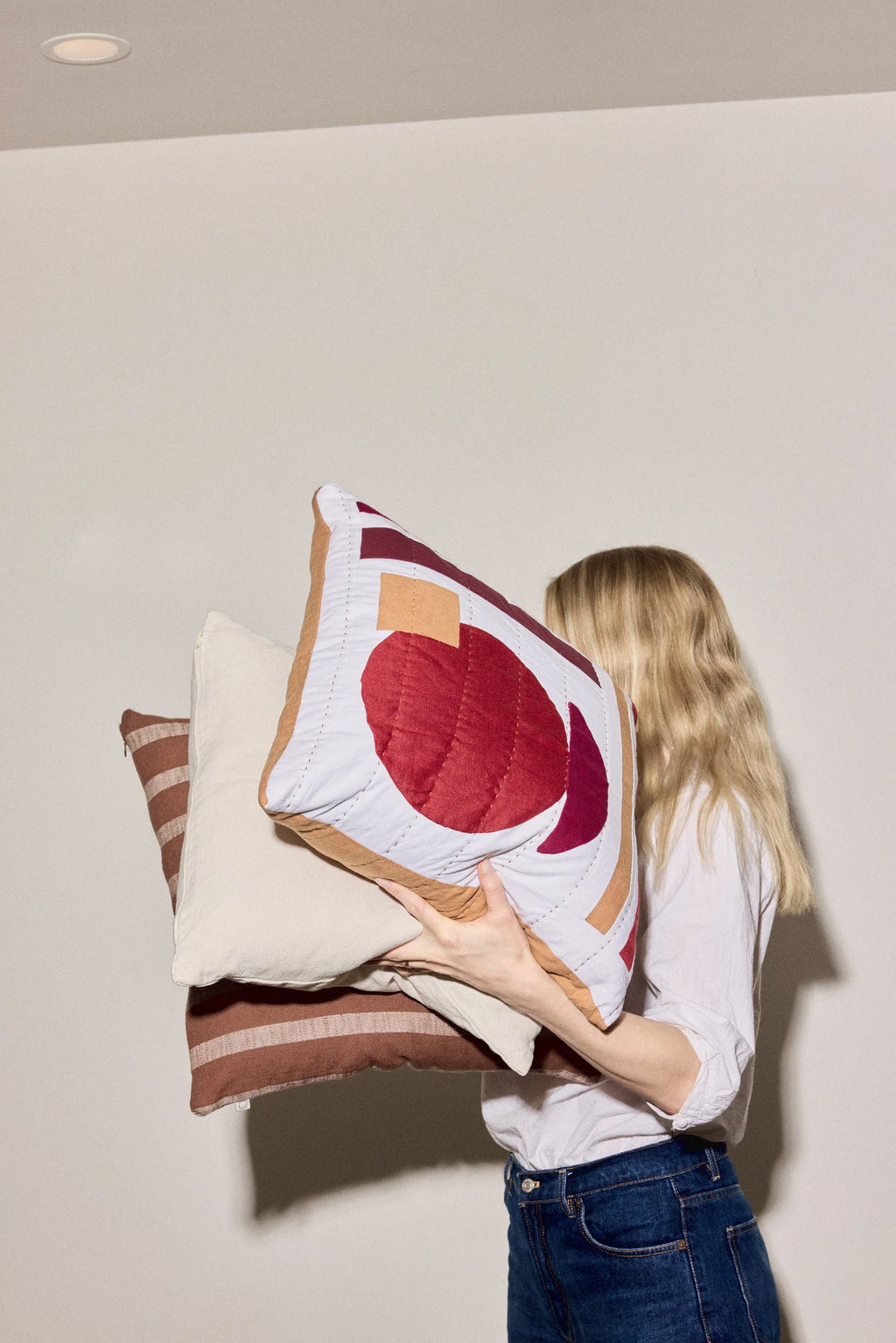 Person holding two decorative pillows against a plain wall
