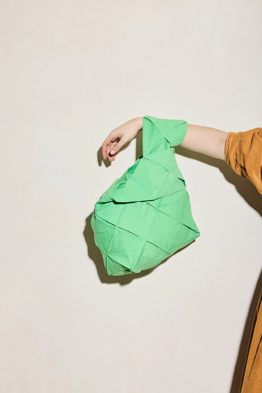 Person holding a green origami-like quilted bag against a plain background