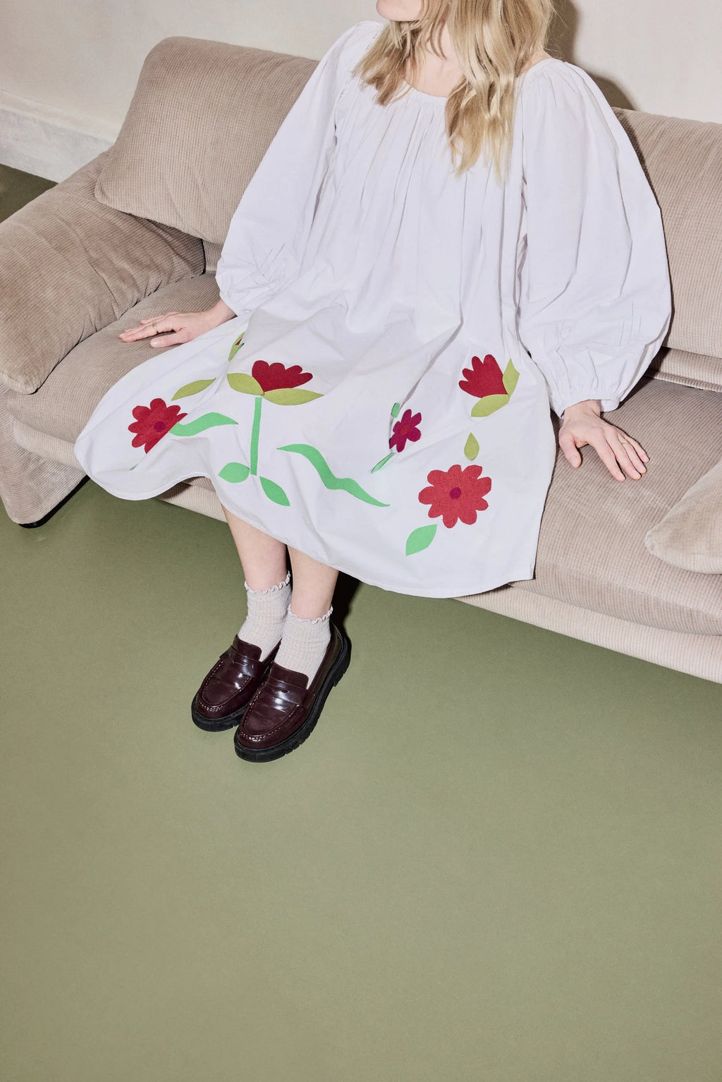 Person wearing a white dress with floral quilted patterns sitting on a beige couch.