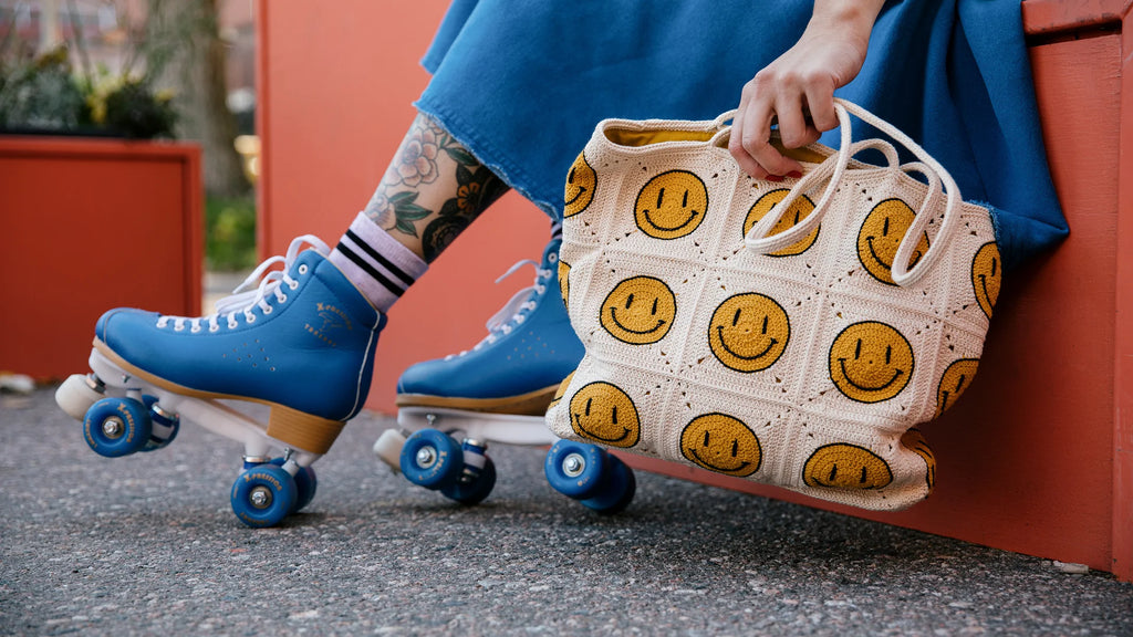 Person wearing blue roller skates holding a crochet bag with smiley face patterns.